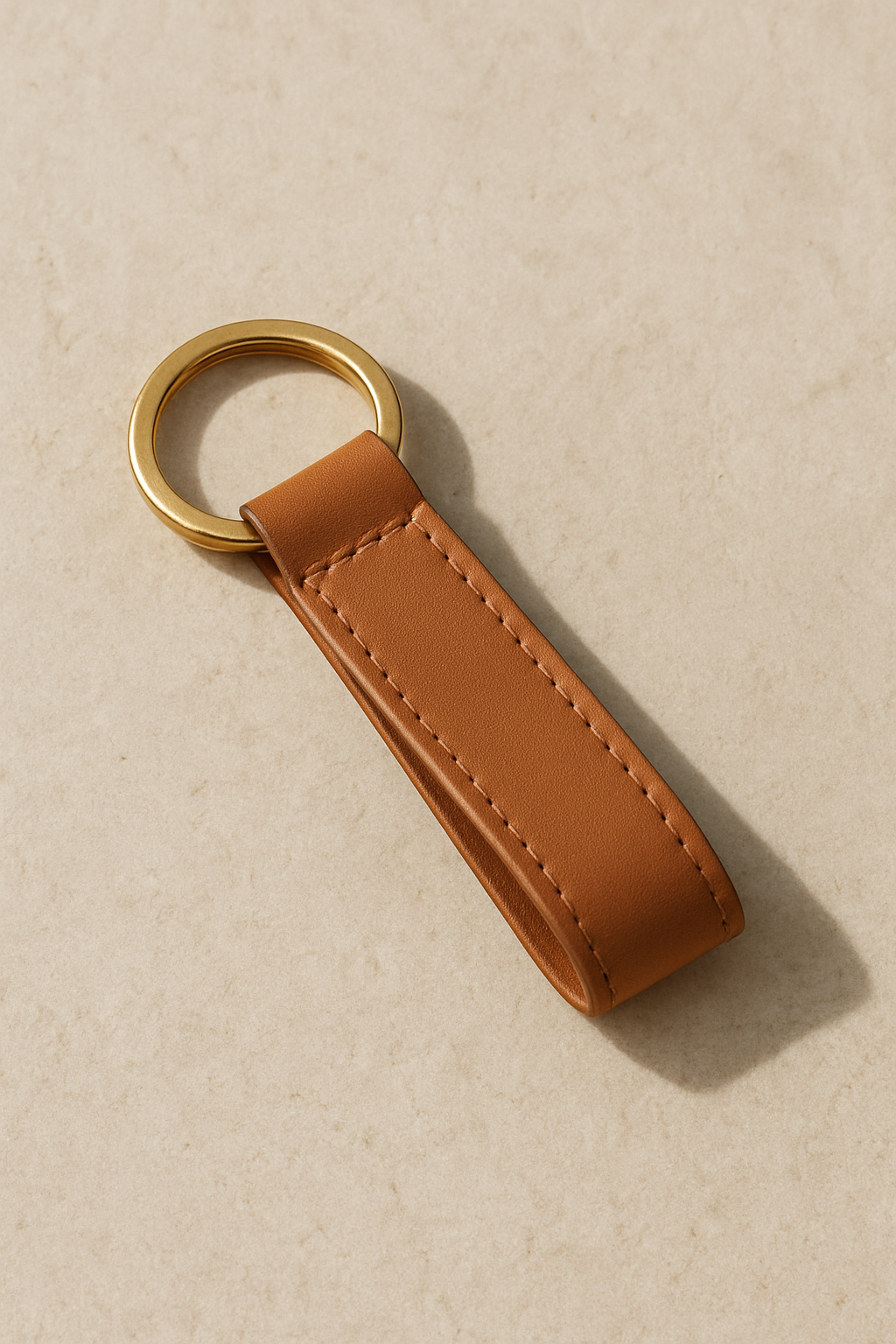 minimalist product image of a premium leather keychain on a stone surface with soft shadows.