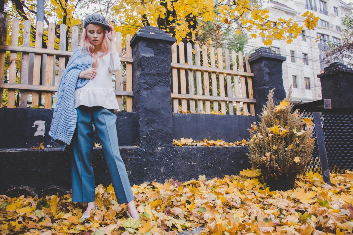 woman standing near fence while stepping on ground covered with withered leaves