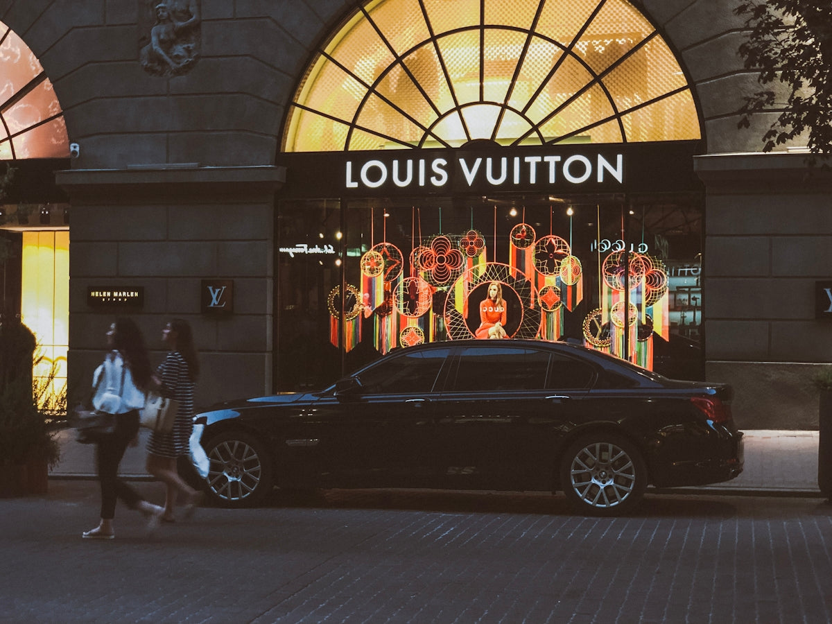 black sedan parking near Louis Vuitton building and two women walking near road