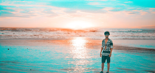 man in black and white jacket standing on sea shore during sunset