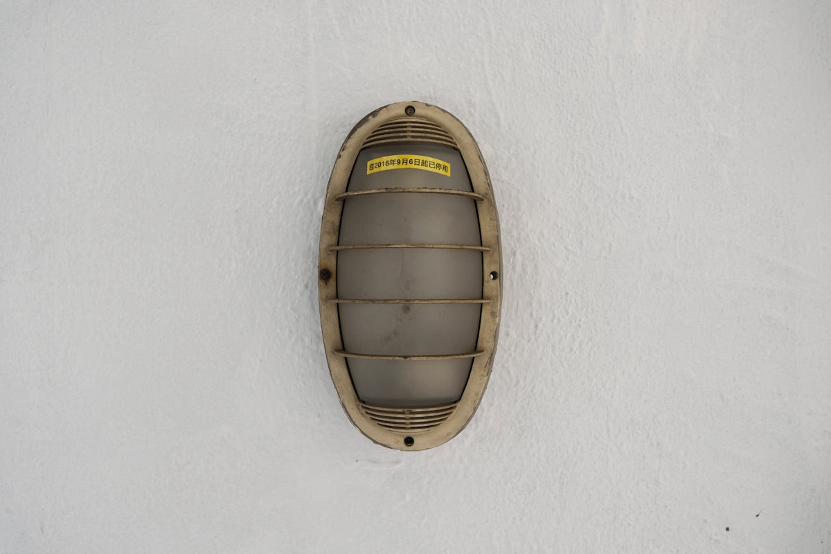 A weathered oval light fixture on a white wall.