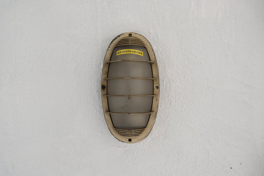 A weathered oval light fixture on a white wall.