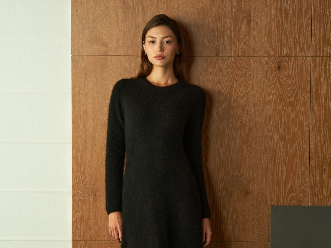 Young woman in a black dress standing against wood paneling.