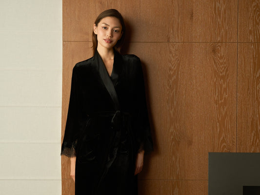 Woman in a black velvet robe standing indoors.