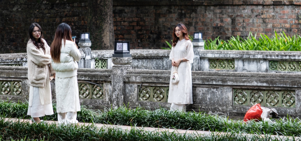 Three women in white outfits stand near stone wall.