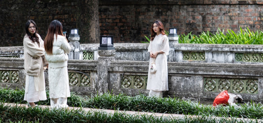 Three women in white outfits stand near stone wall.