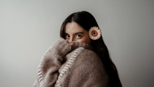 Woman peeking over a cozy sweater with flower accessory.