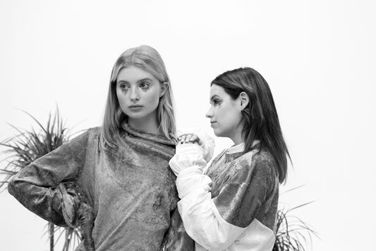Two women in stylish velvet tops, one adjusting the other.
