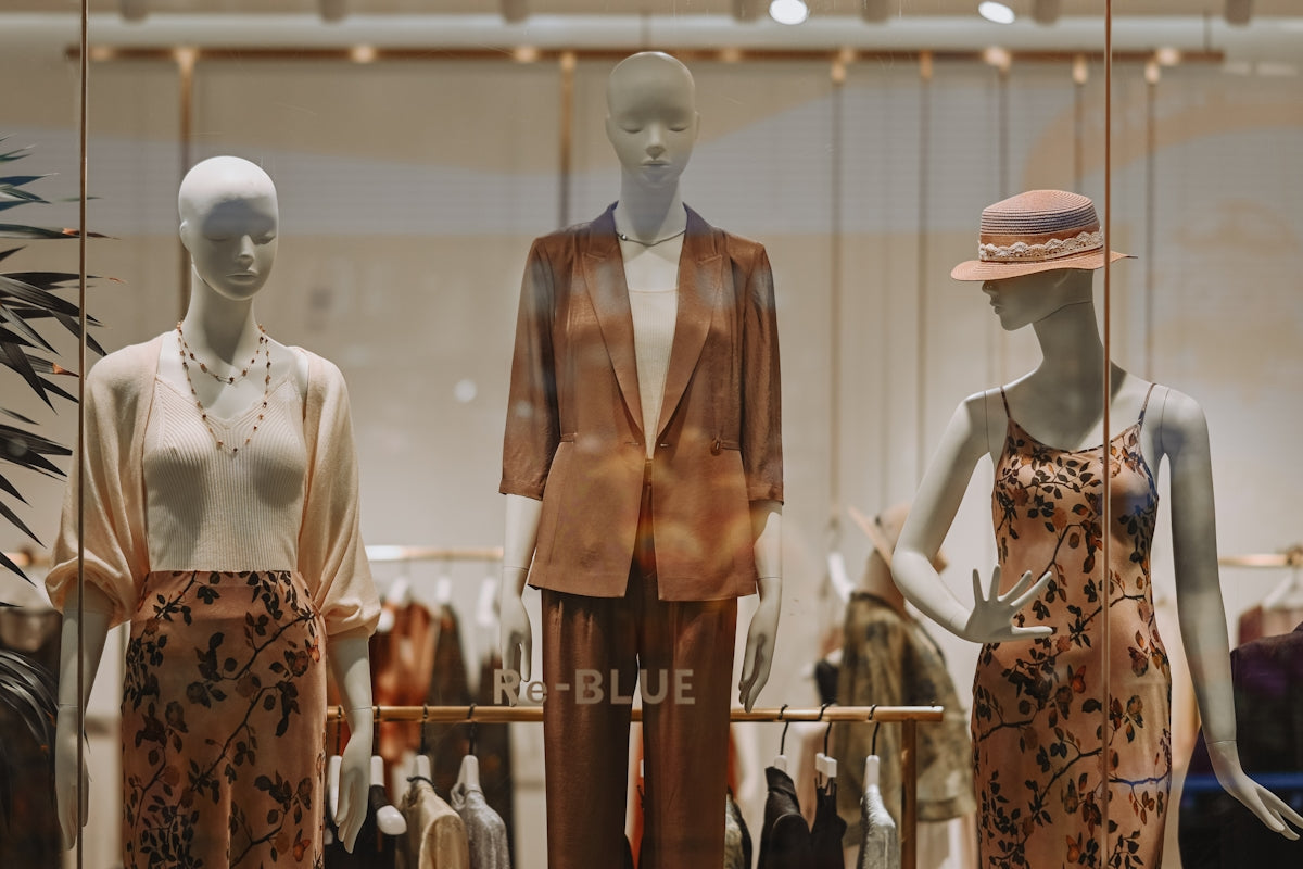 Three mannequins display fashionable clothing in a store window.