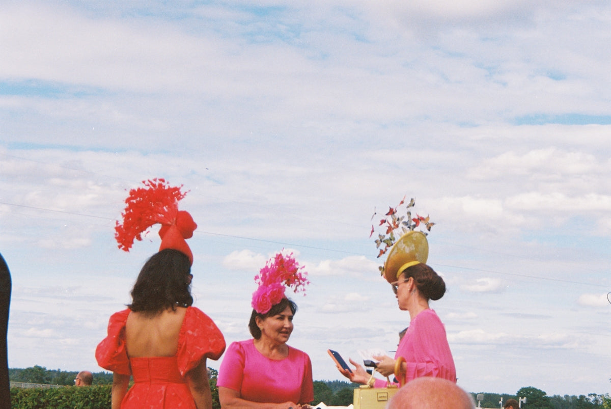 Women in vibrant dresses and elaborate hats outdoors