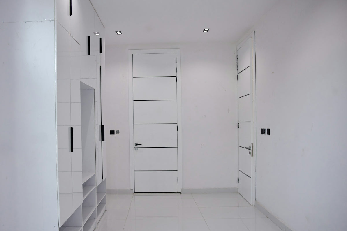 A minimalist hallway with white walls, glossy white doors, and black hardware