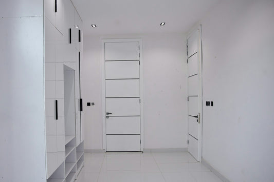 A minimalist hallway with white walls, glossy white doors, and black hardware