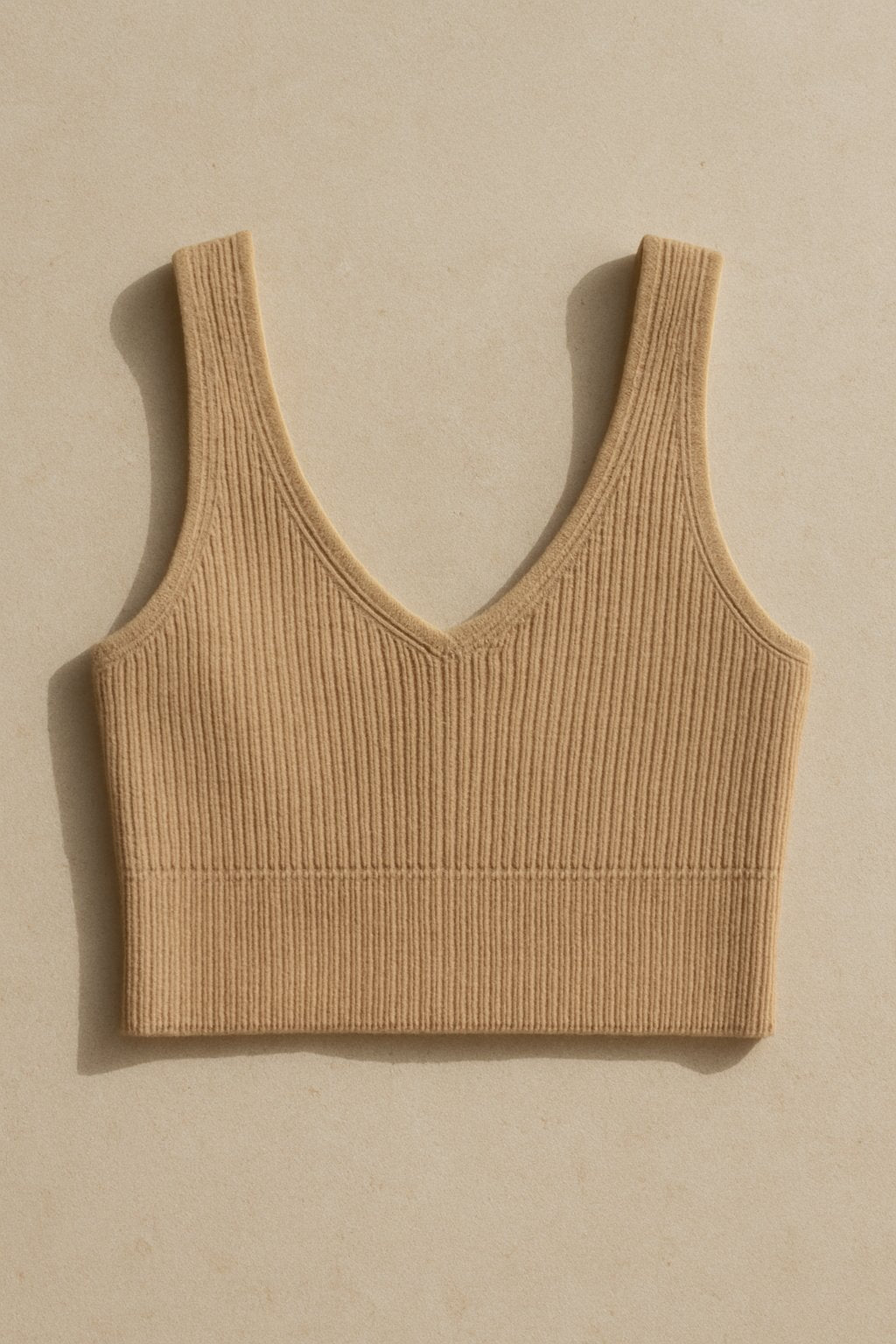 minimal flat lay of a trendy cropped knit top in neutral tones, styled on a beige stone background with clean light.